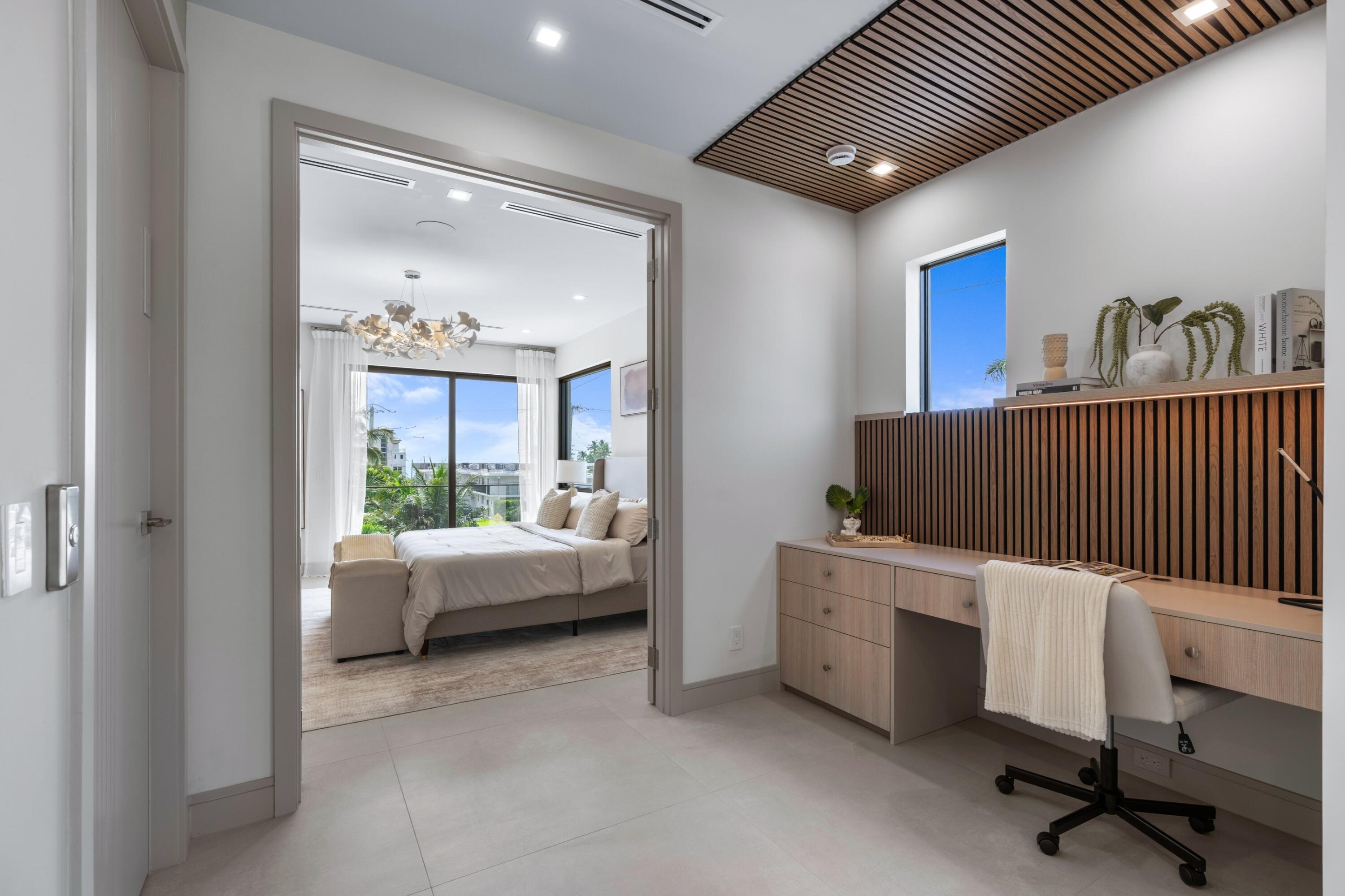 Modern bedroom with a wood-slat ceiling and built-in desk, viewed through an open doorway.