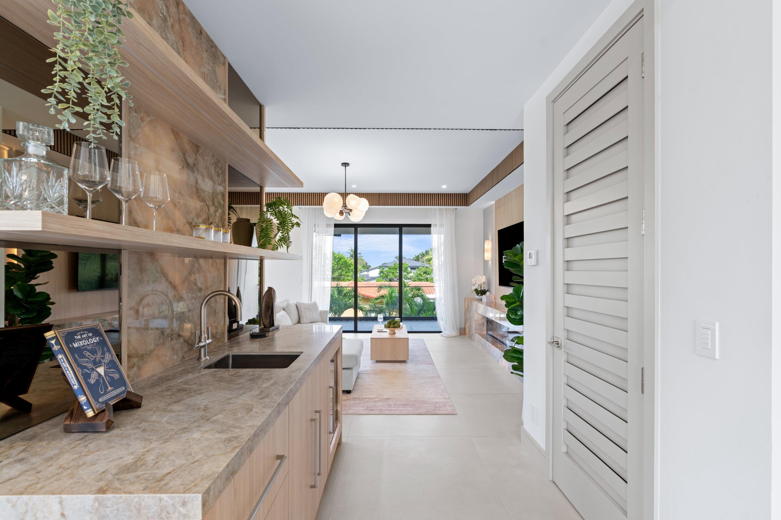 Open kitchen and living room with stone counters, wood cabinetry, and sliding glass doors to greenery.