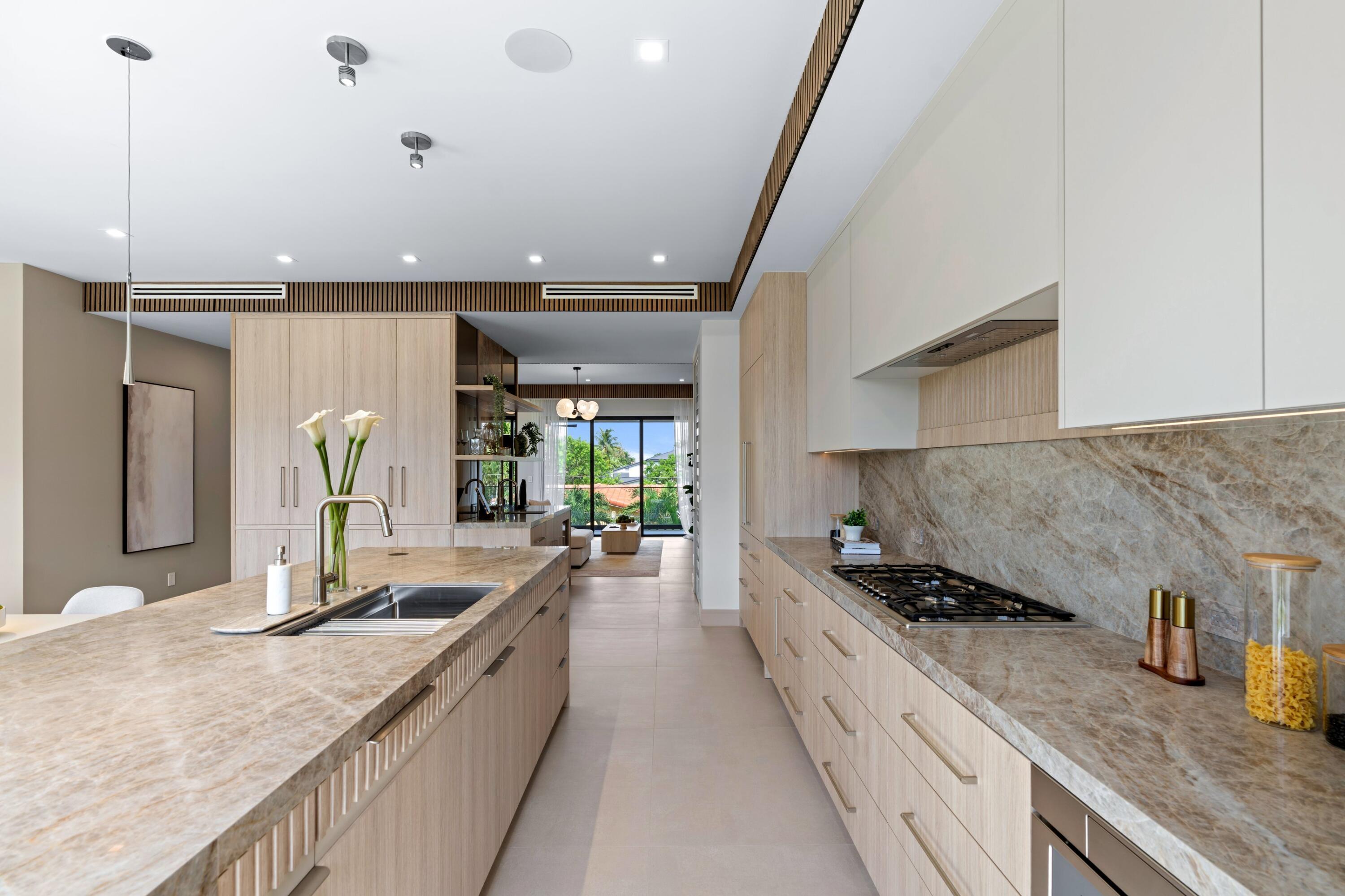 Modern kitchen with stone countertops, pale wood cabinetry, a large island, and garden views through sliding doors.