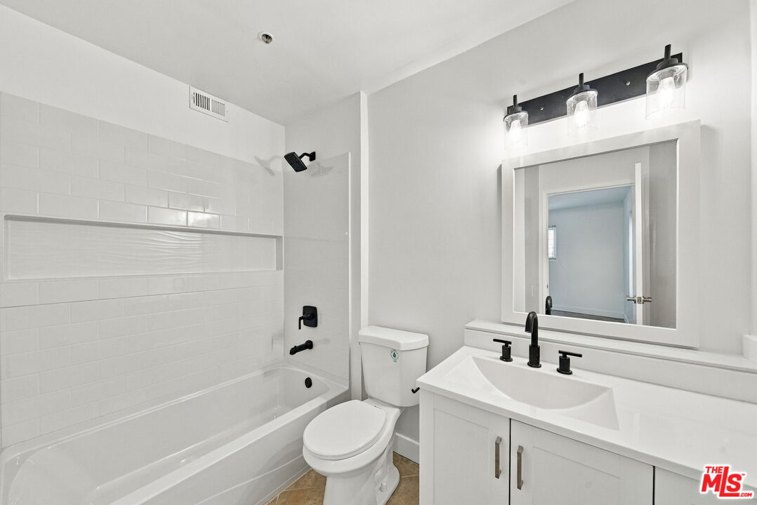 Bathroom with a white tiled tub-shower, toilet, and vanity with black fixtures.