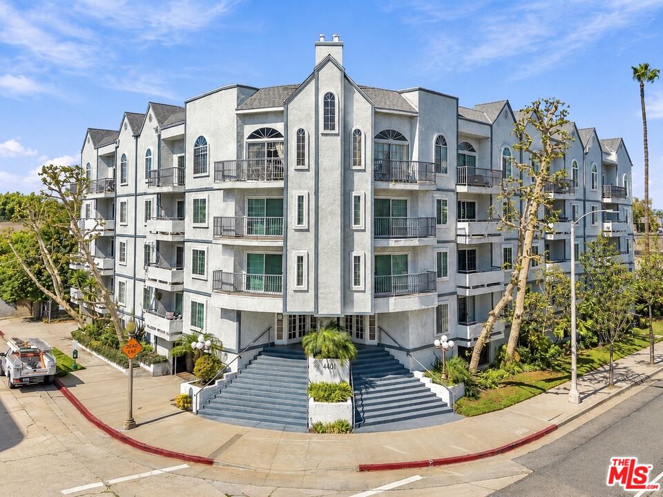 Multi-story residential building with gray façade, arched windows, balconies, and wide front steps.