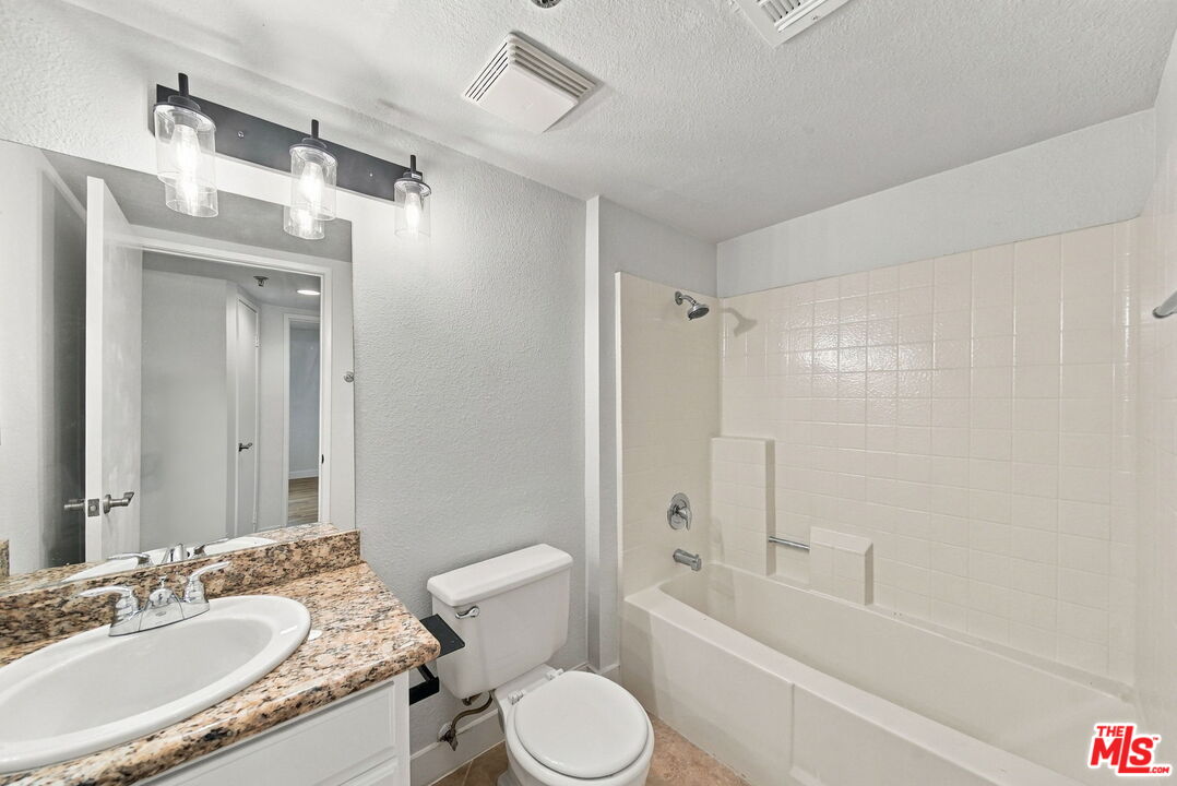 Bathroom with a tiled tub and shower, toilet, and granite vanity.