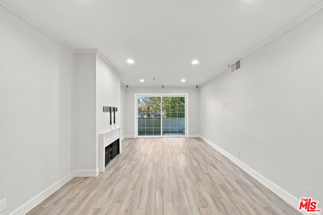 Empty living room with light wood-look floors, a fireplace, and sliding glass doors to a balcony.