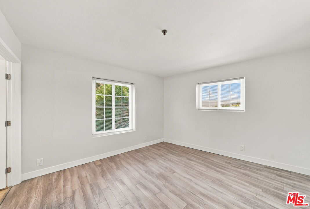 Empty room with light wood-look flooring and two windows with blinds.
