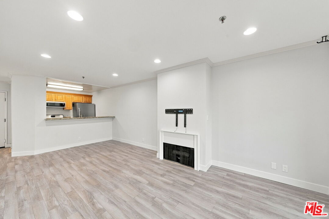 Vacant living room with gray wood-look floors, a fireplace, and an open kitchen.