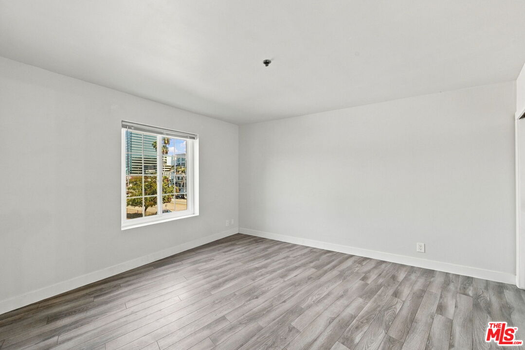 Empty room with gray plank flooring and a window overlooking buildings and palm trees.