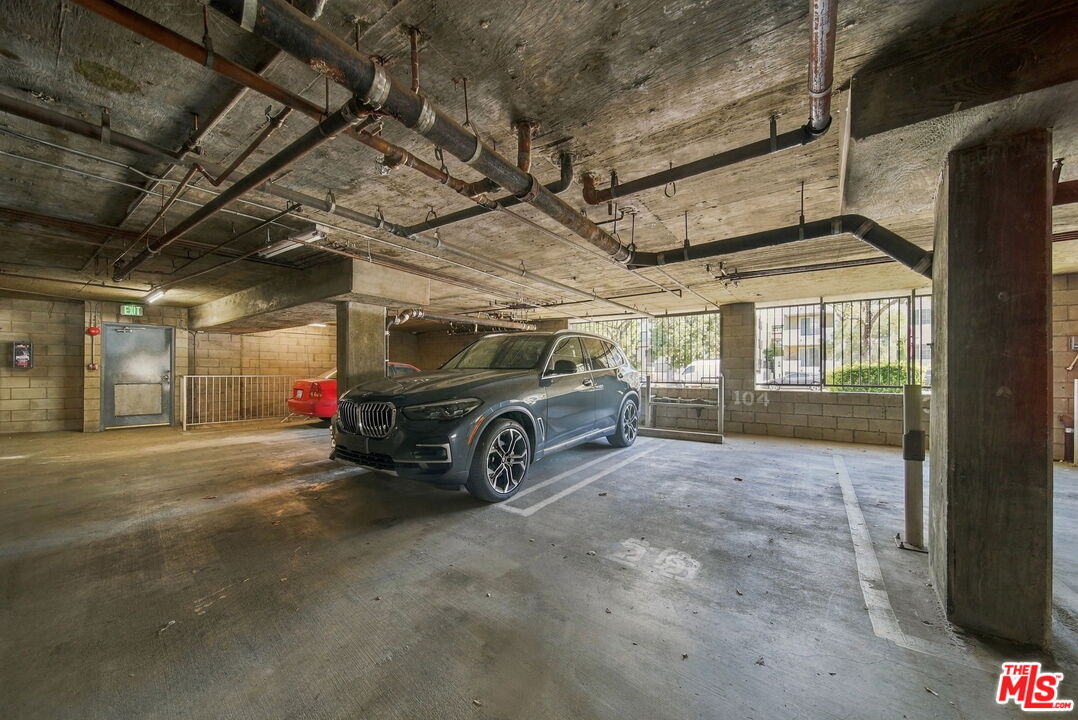Concrete parking garage with exposed ceiling pipes and a dark SUV in a marked space.