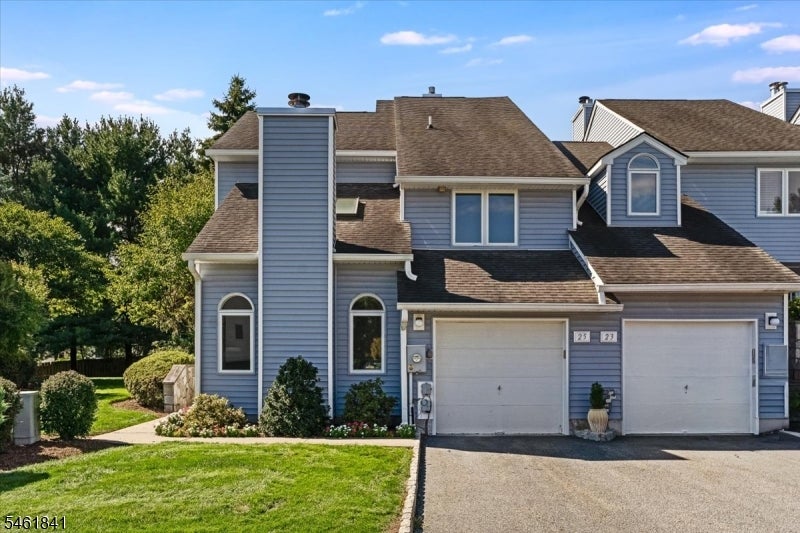 Blue-gray attached home with two garage doors, arched windows, and a landscaped front lawn.