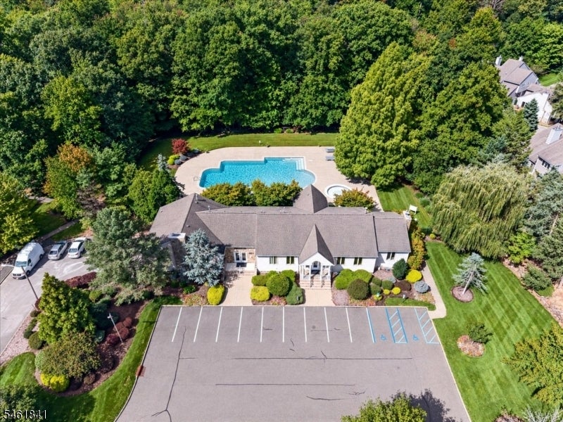 Aerial view of a single-story home with a backyard pool, mature trees, and paved parking.