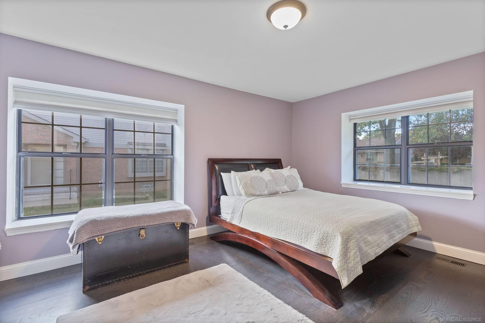 Bedroom with a dark wood platform bed, lavender walls, and two large windows.