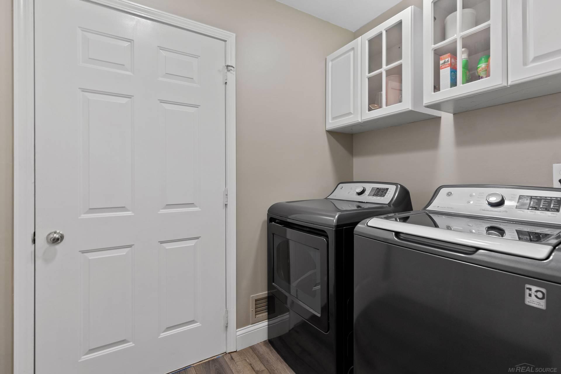 Laundry room with dark washer and dryer beneath white upper cabinets.