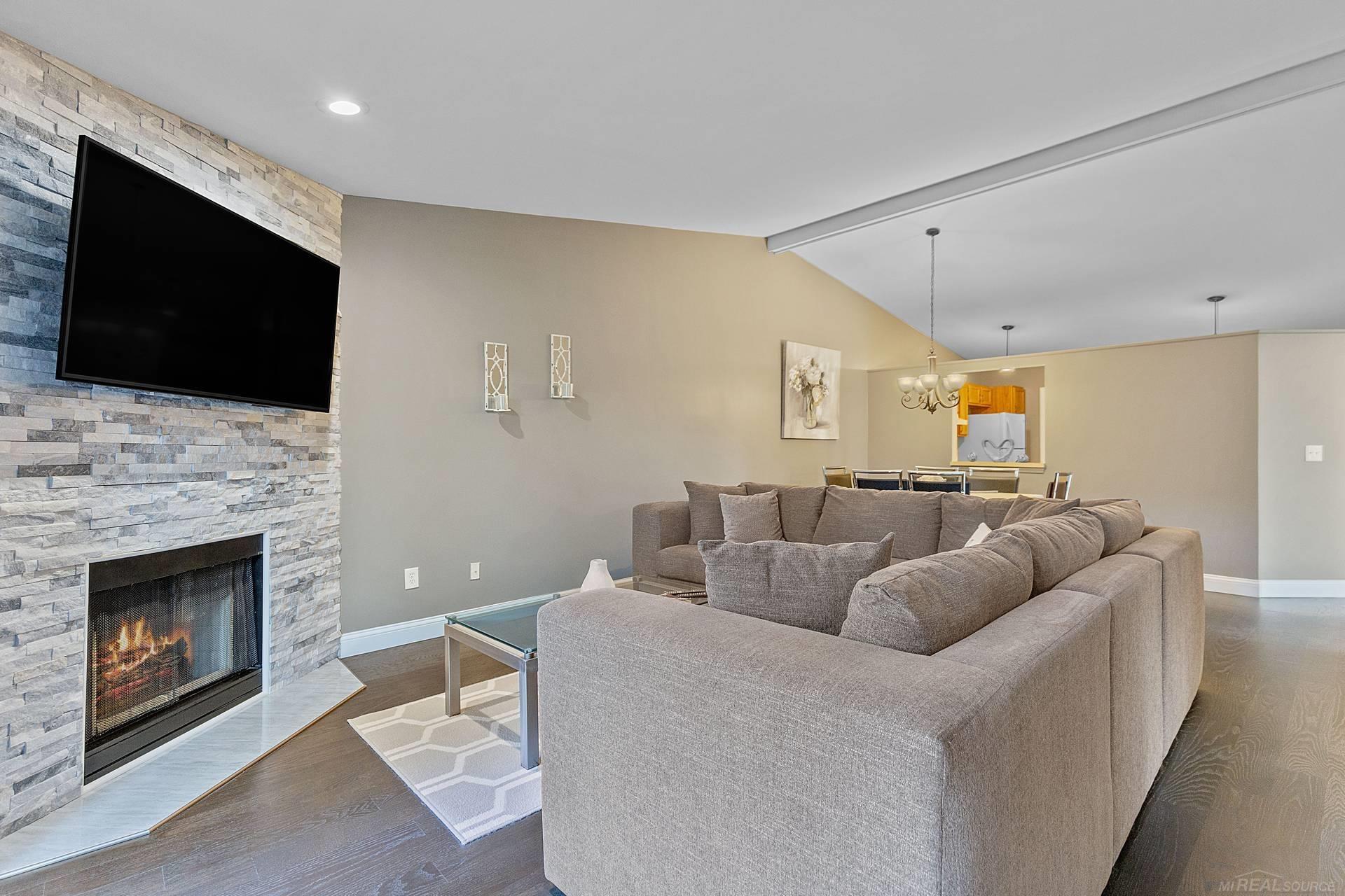 Living room with a gray sectional, stone fireplace, and wall-mounted television.