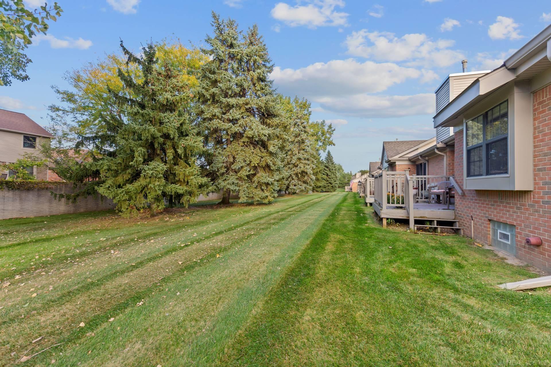Grassy lawn beside brick homes with raised decks and mature evergreen trees.