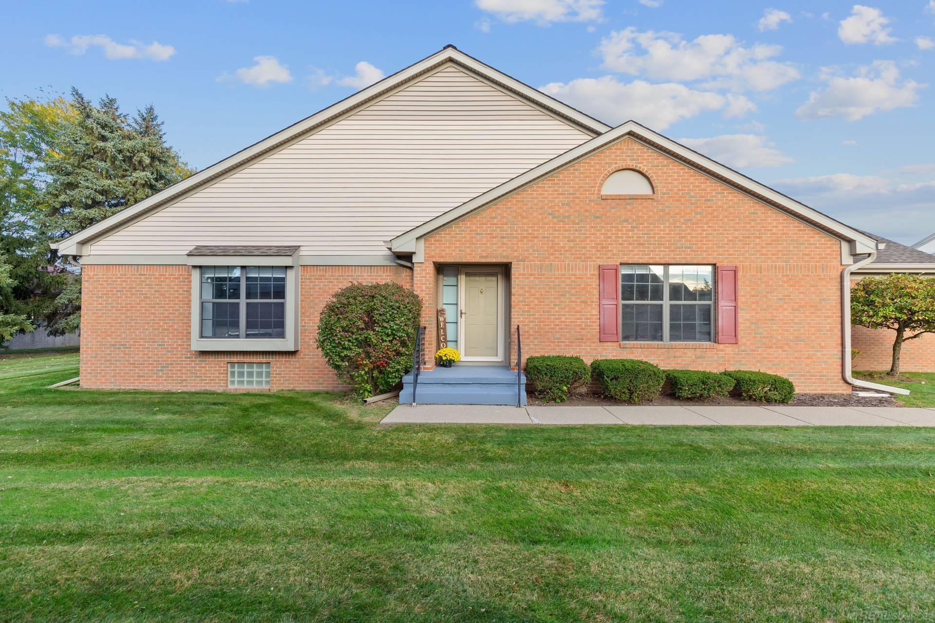 Brick house with a large gabled roof, red shutters, blue entry steps, and landscaped front lawn.