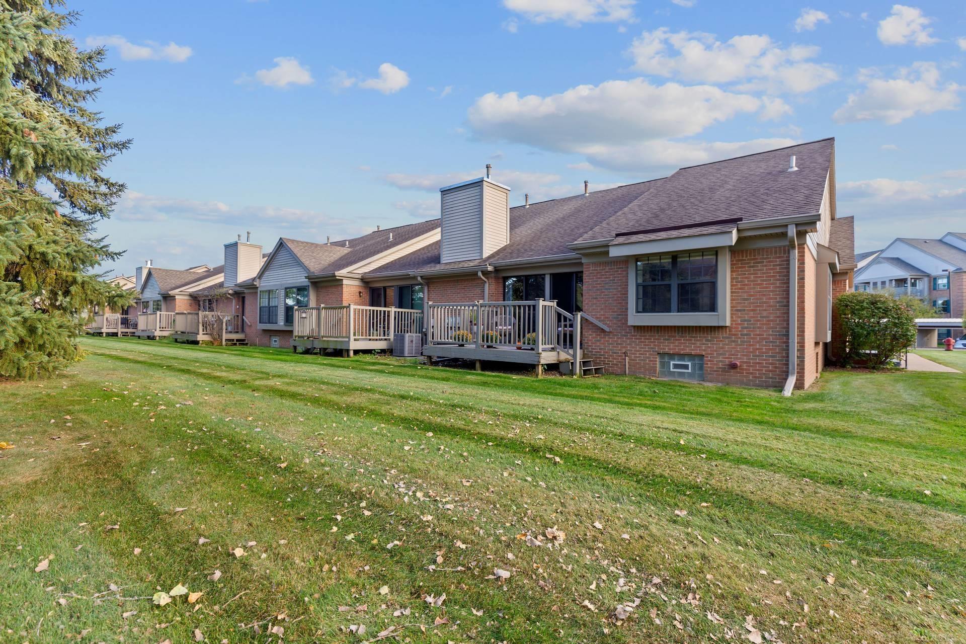 Brick condominiums with raised wooden decks line a broad lawn beneath a blue sky.