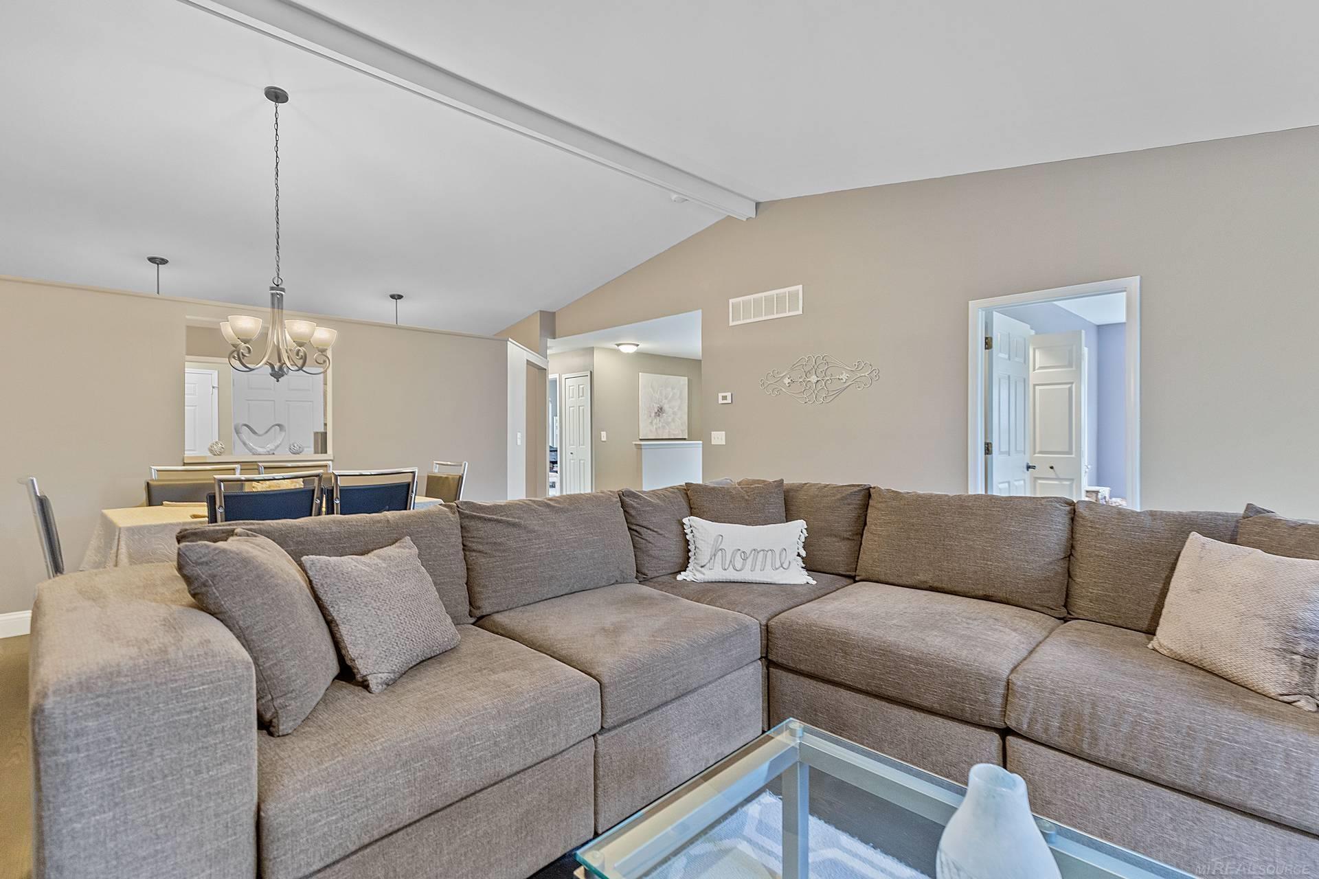 Living room with a large gray sectional, glass coffee table, and dining area beyond.