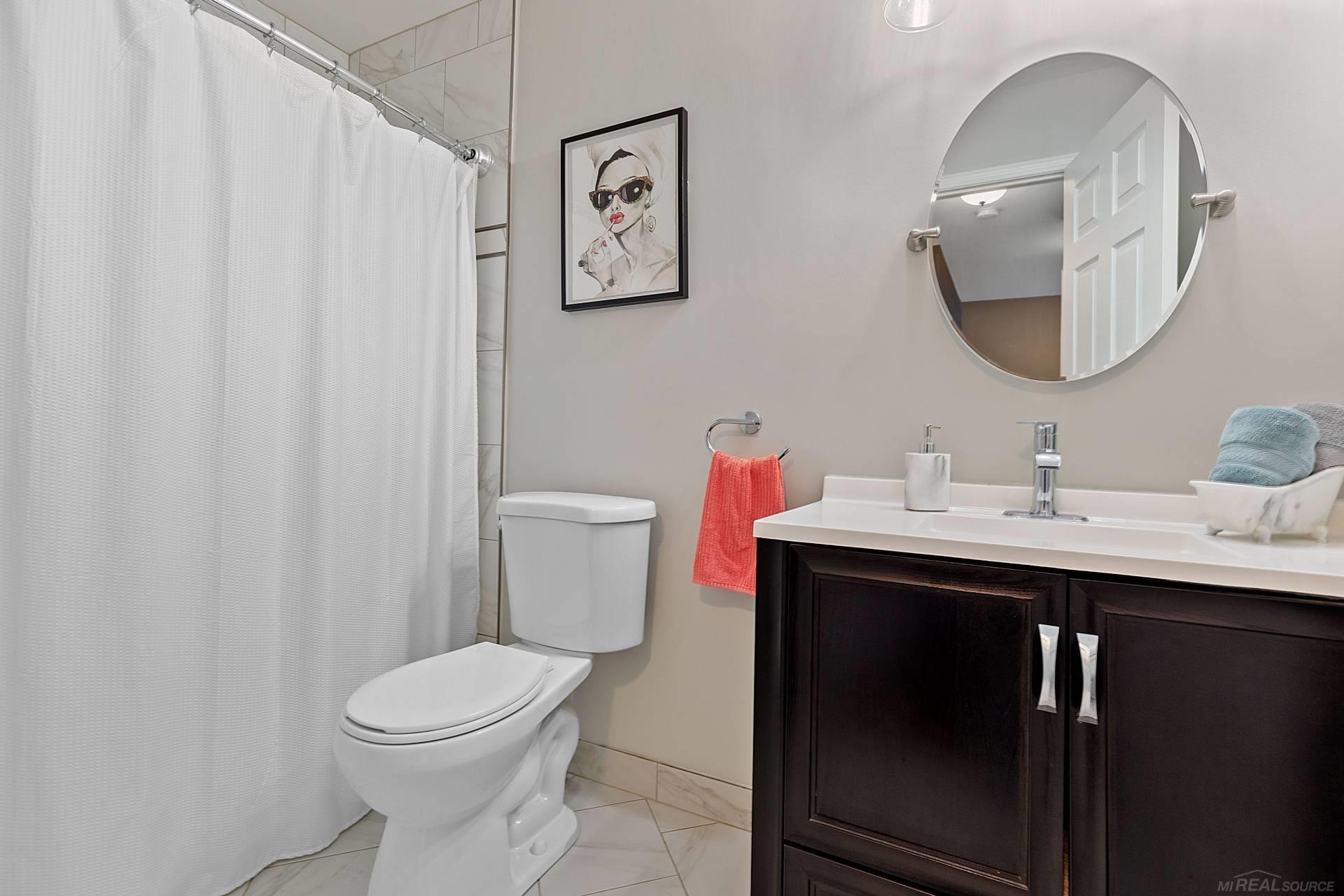 Bathroom with a dark wood vanity, round mirror, white shower curtain, and toilet.