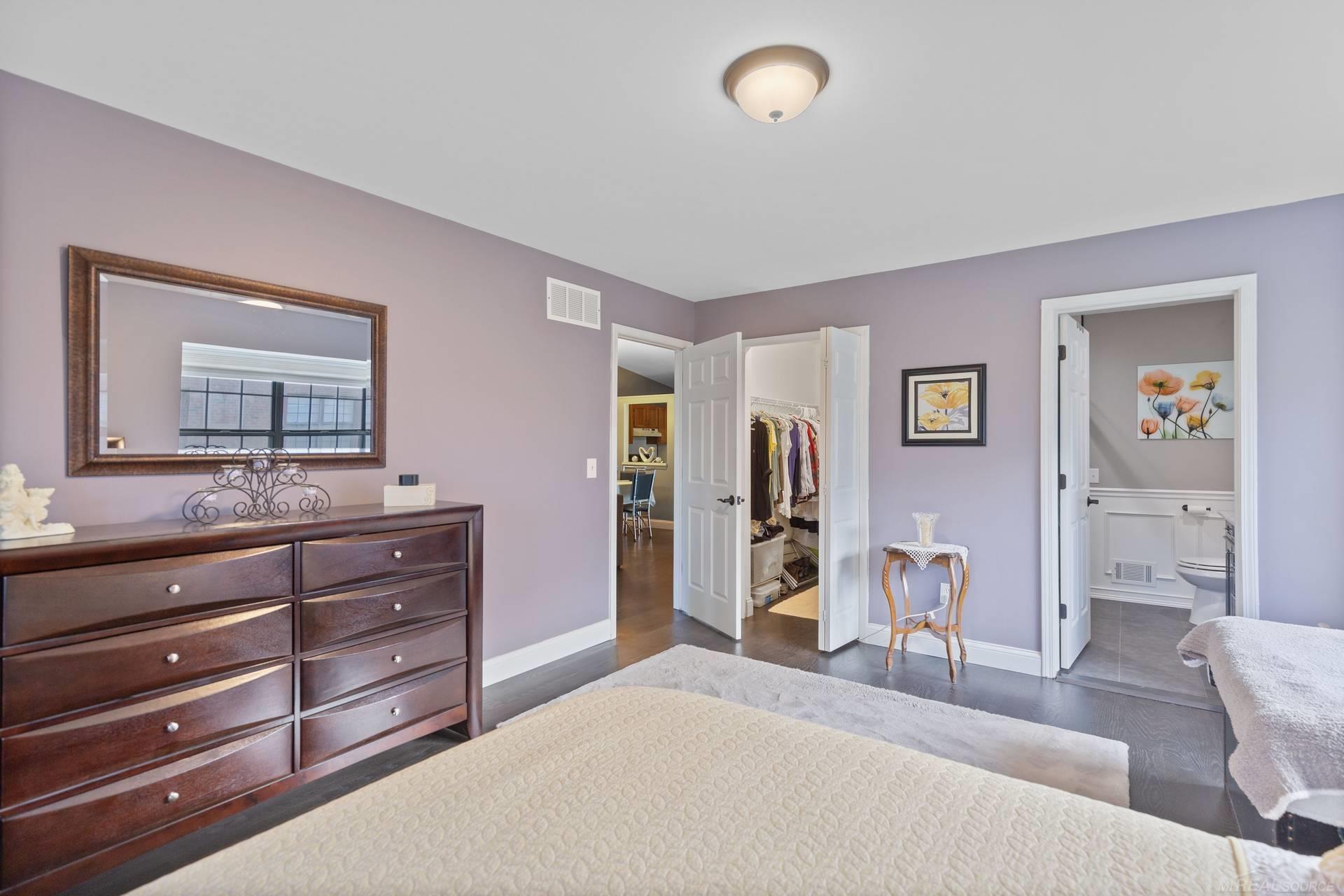 Bedroom with lavender walls, a dark wood dresser, and open doors to a closet and bathroom.