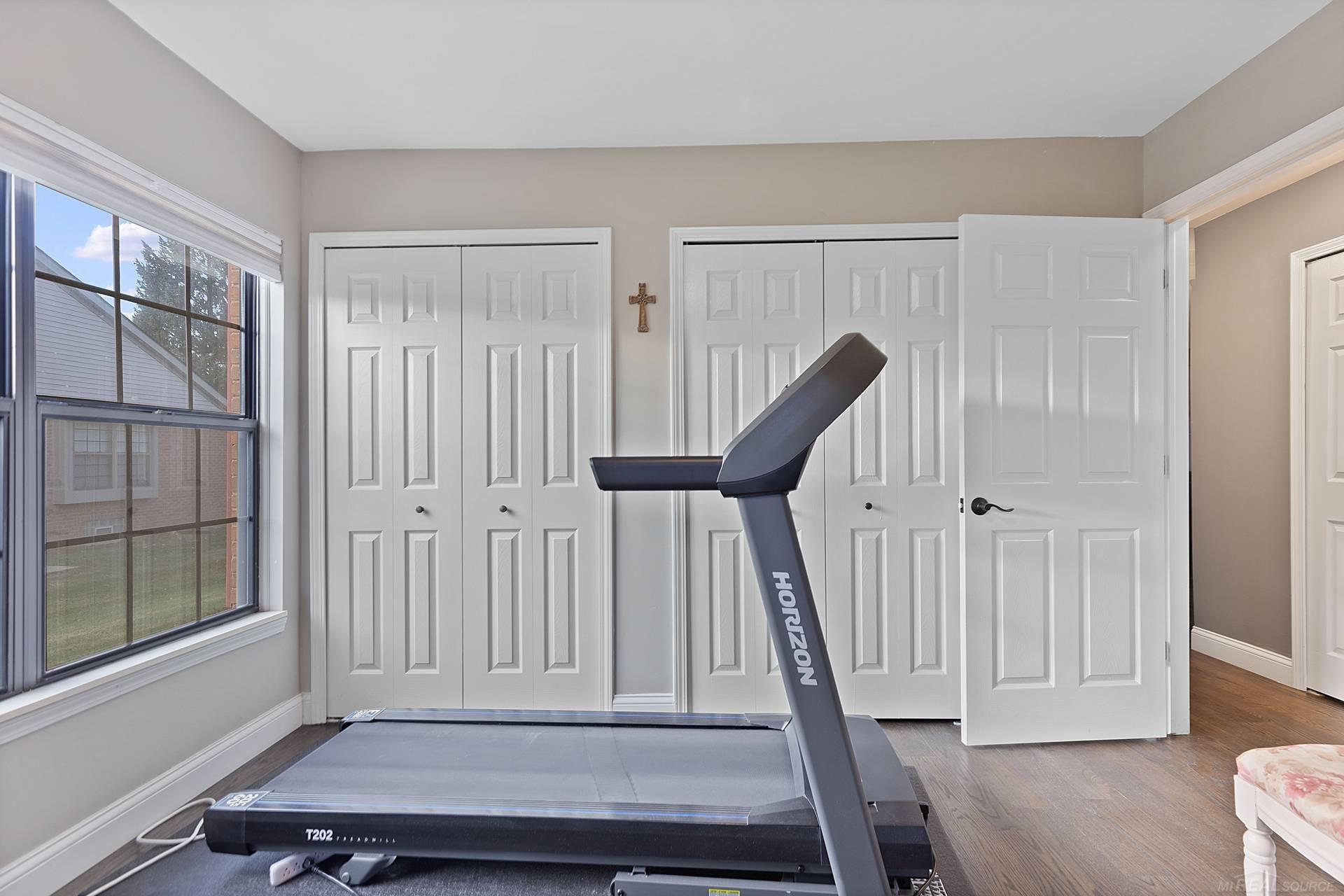 Home exercise room with a Horizon treadmill, paneled closet doors, and a large window.
