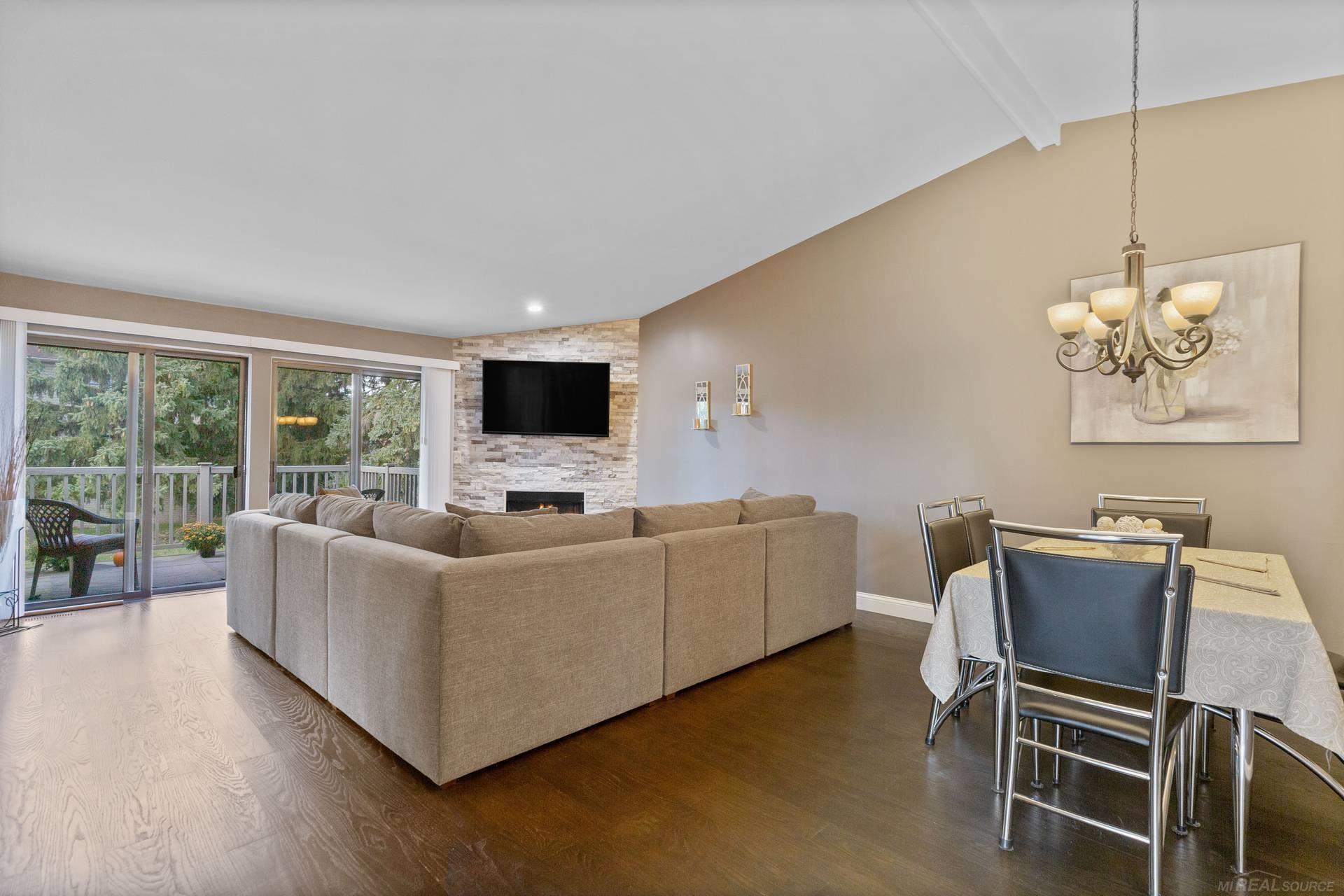 Living and dining area with a stone fireplace, sectional sofa, and sliding doors to a deck.