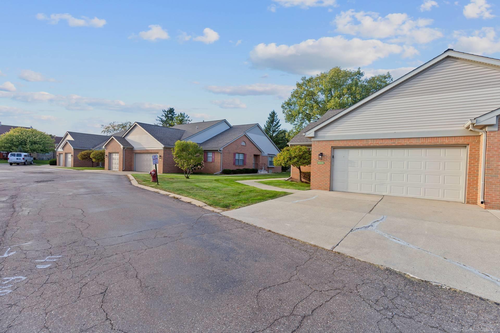 Brick residence with a double garage beside a paved lane and neighboring homes.