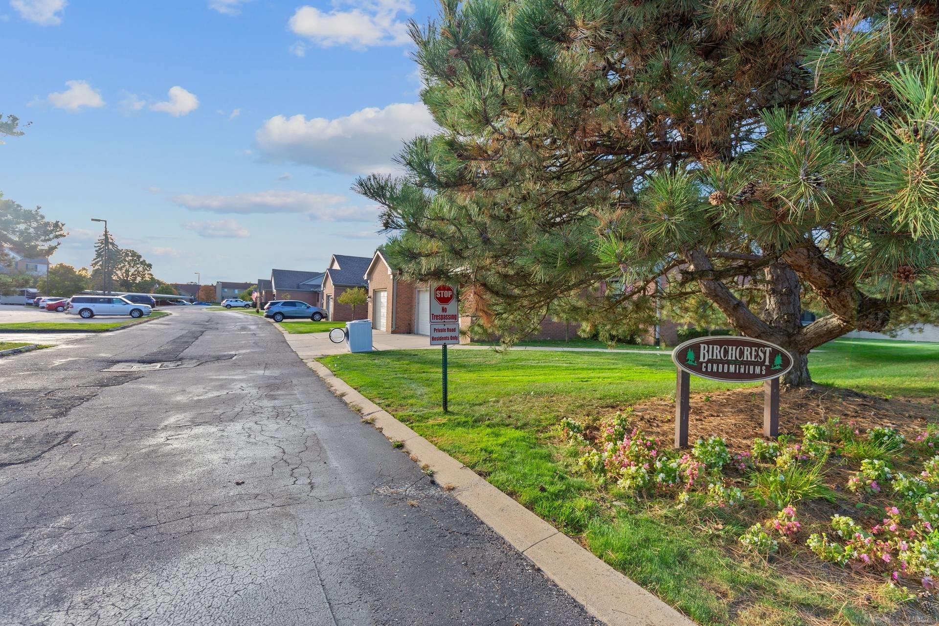 Birchcrest Condominiums private drive, marked by a roadside sign beneath a large pine tree.