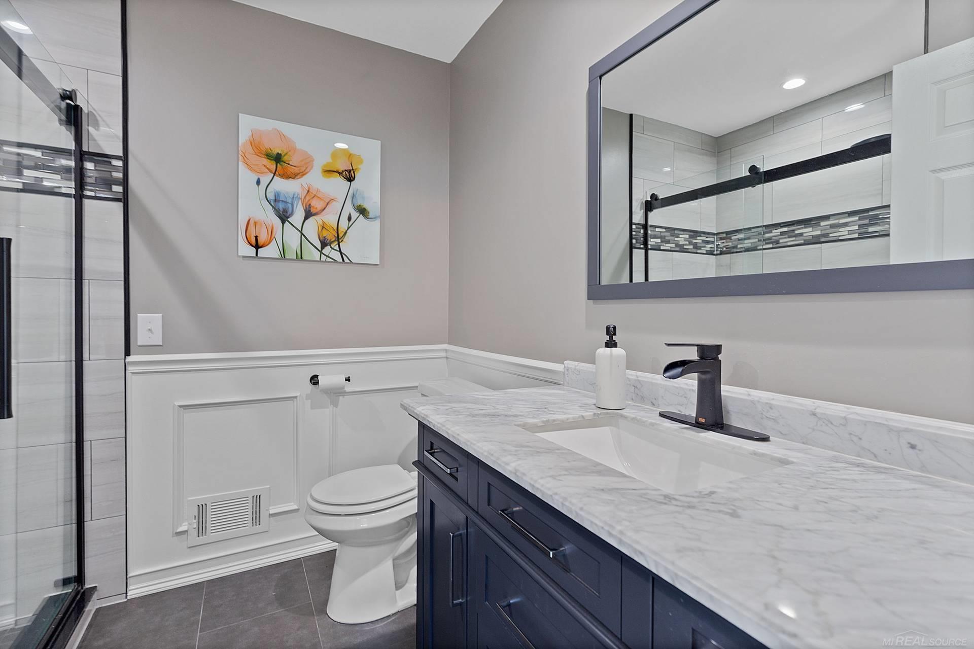Renovated bathroom with a glass shower, navy vanity, marble-look counter, and floral wall art.