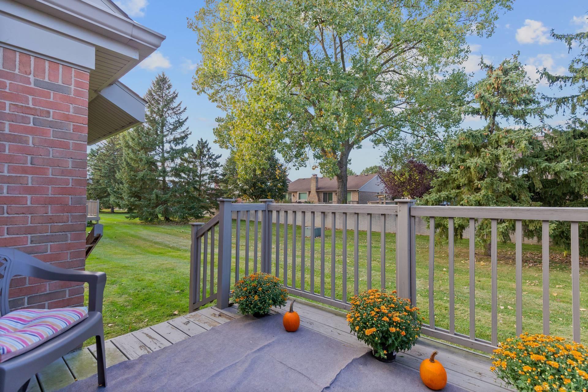 Raised backyard deck with gray railings, potted flowers, and pumpkins overlooking a tree-lined lawn.