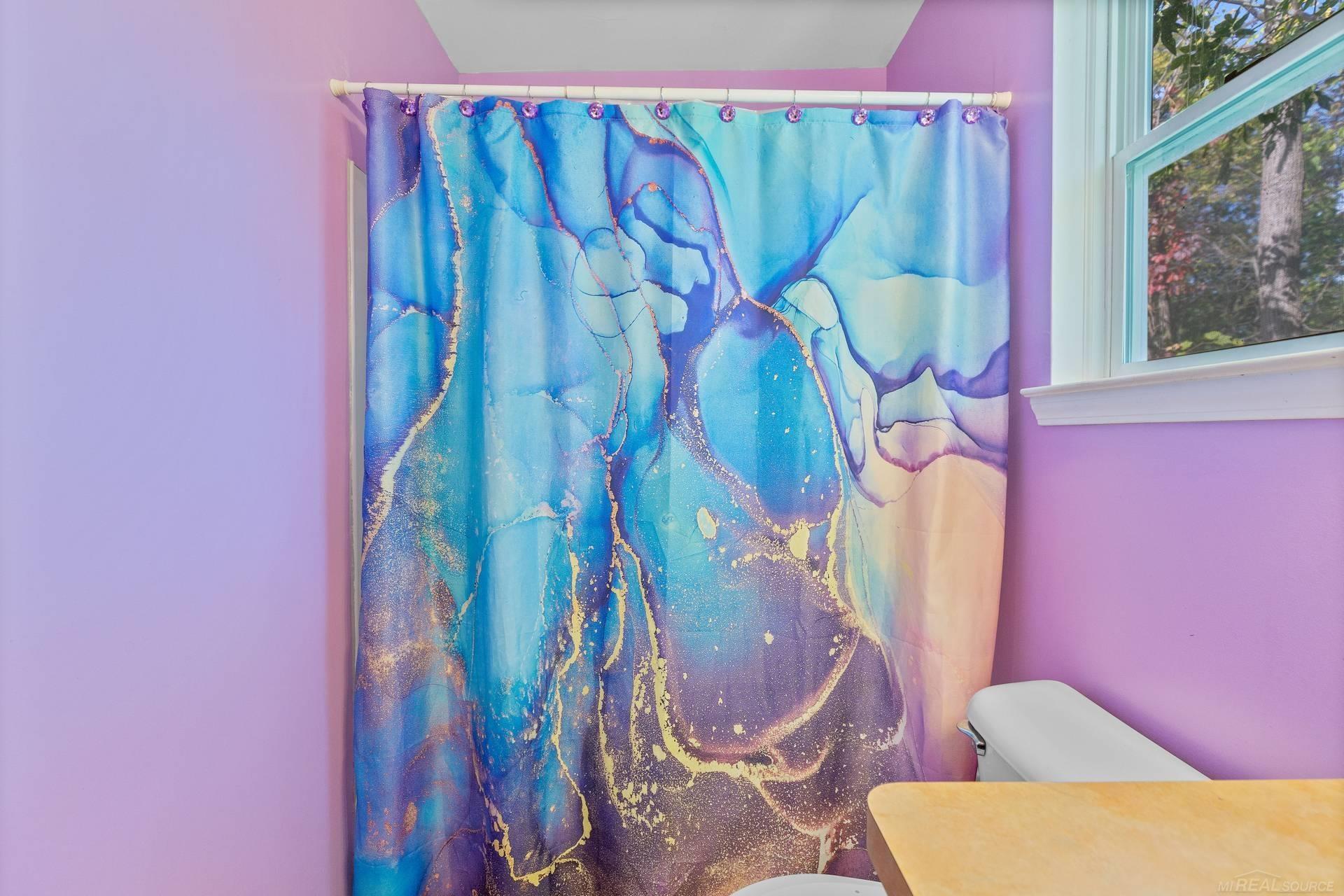 Bathroom with a vivid blue and purple shower curtain, lavender walls, and a window.