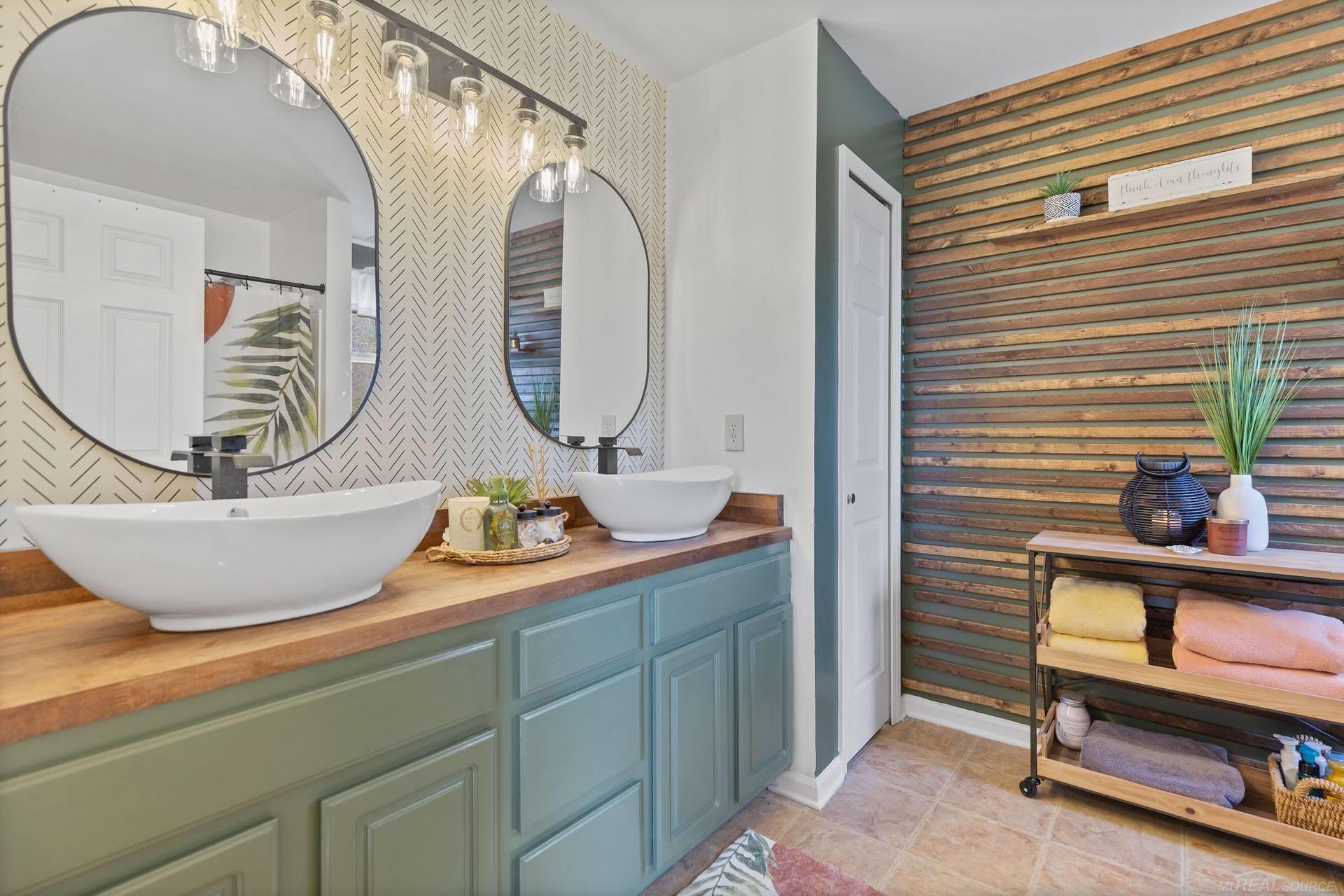 Bathroom with two vessel sinks, teal cabinetry, arched mirrors, and a wood-slat accent wall.