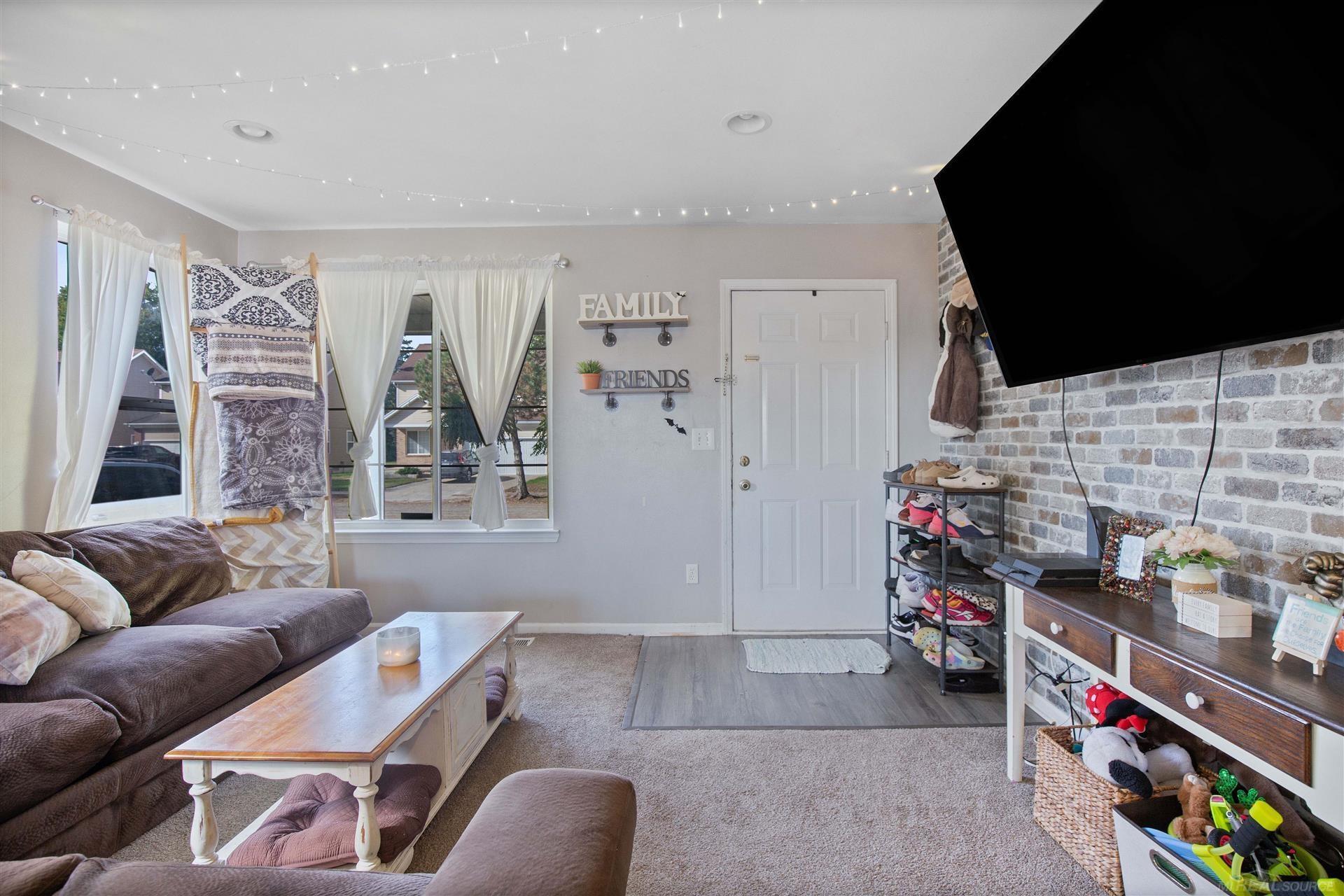 Living room with a gray sectional, curtained windows, ceiling string lights, and a brick wall with a mounted TV.