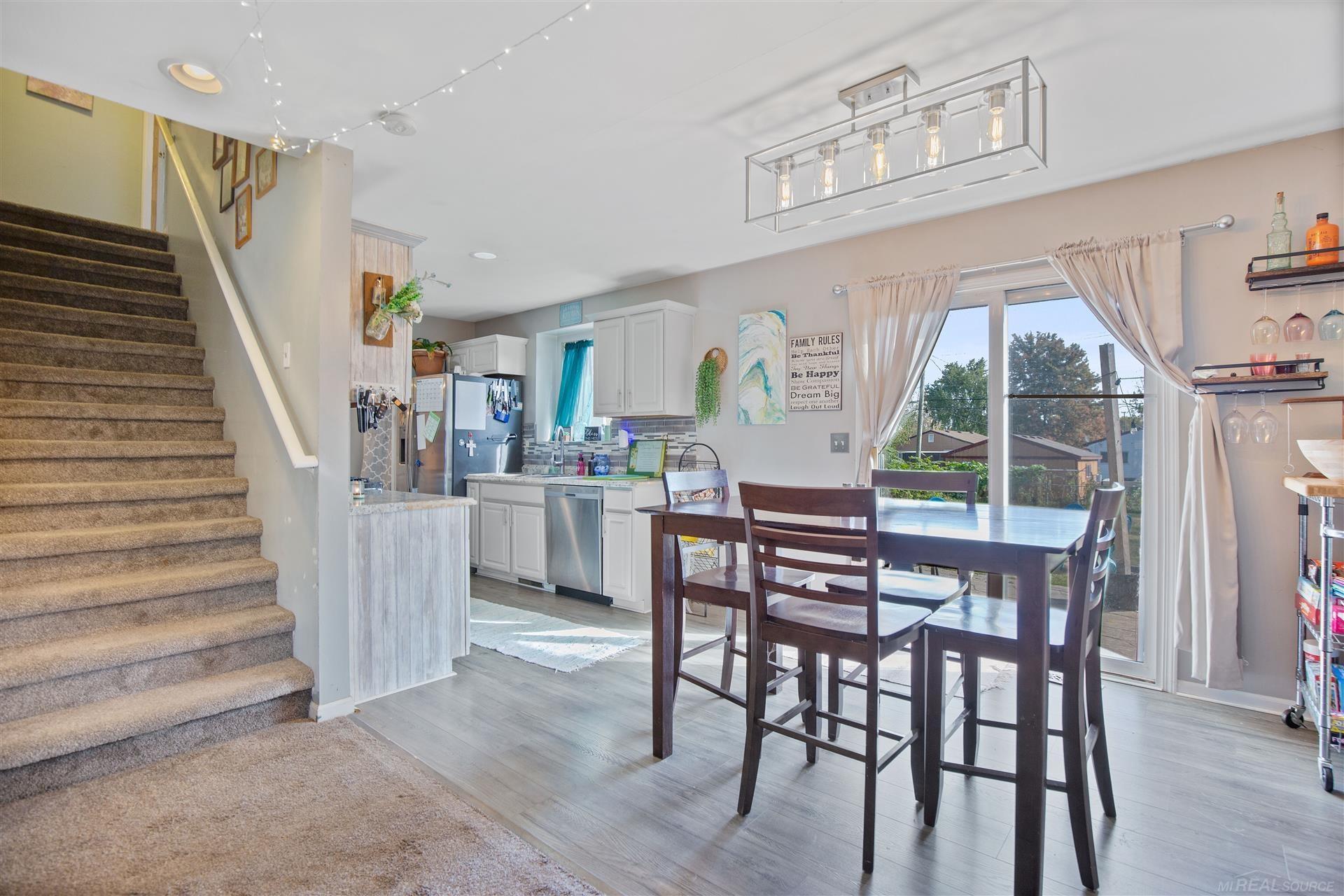 Open kitchen and dining area with white cabinets, dark wood table, sliding doors, and carpeted stairs.