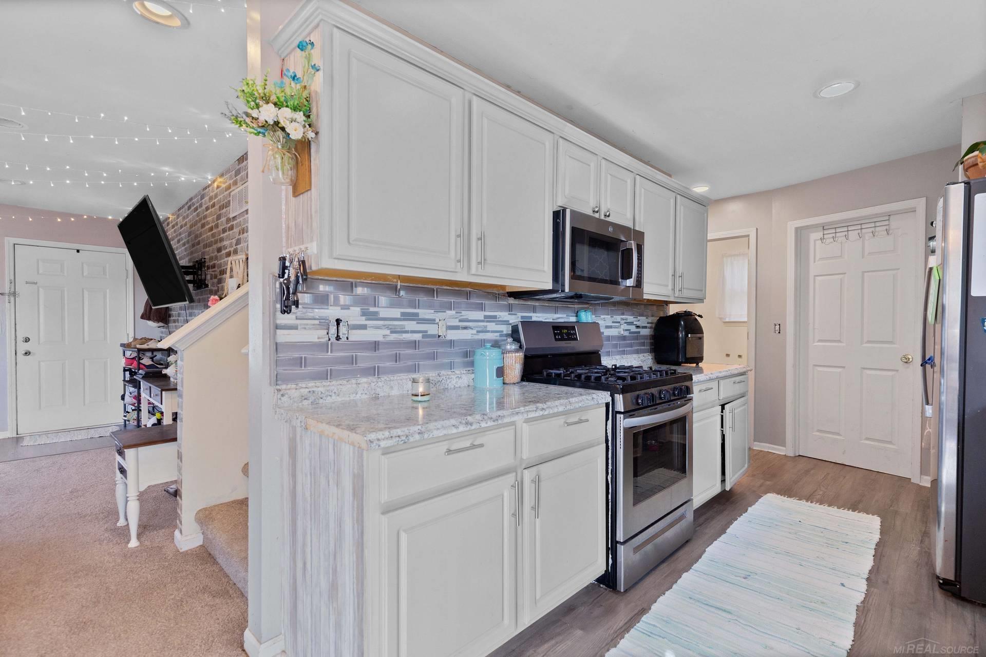 Kitchen with white cabinets, gray tile backsplash, granite counters, and stainless steel gas range.