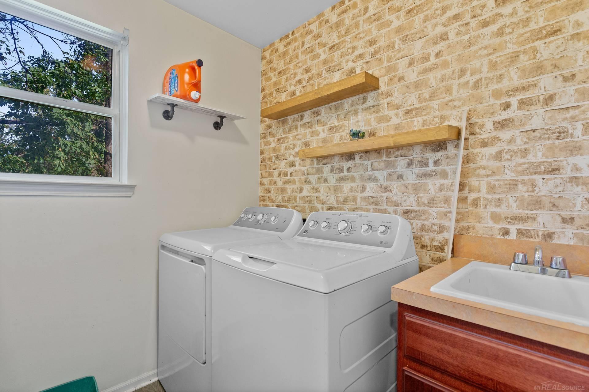 Laundry room with a washer and dryer beside a sink and brick accent wall.