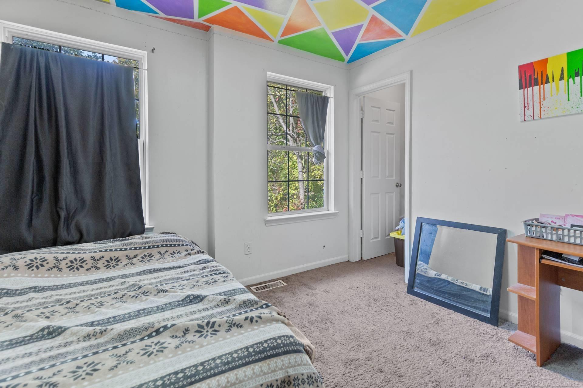 Bedroom with a patterned bedspread, two windows, and a colorful geometric ceiling.