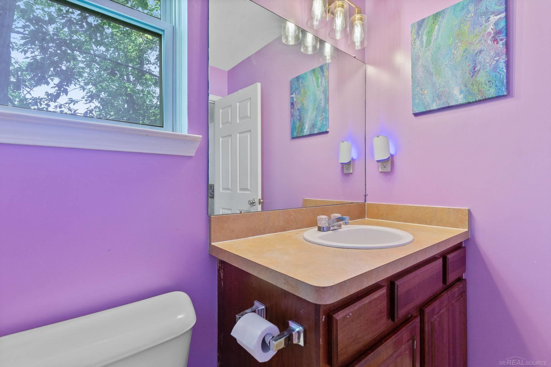 Bathroom with purple walls, dark wood vanity, oval sink, large mirror, and window overlooking trees.