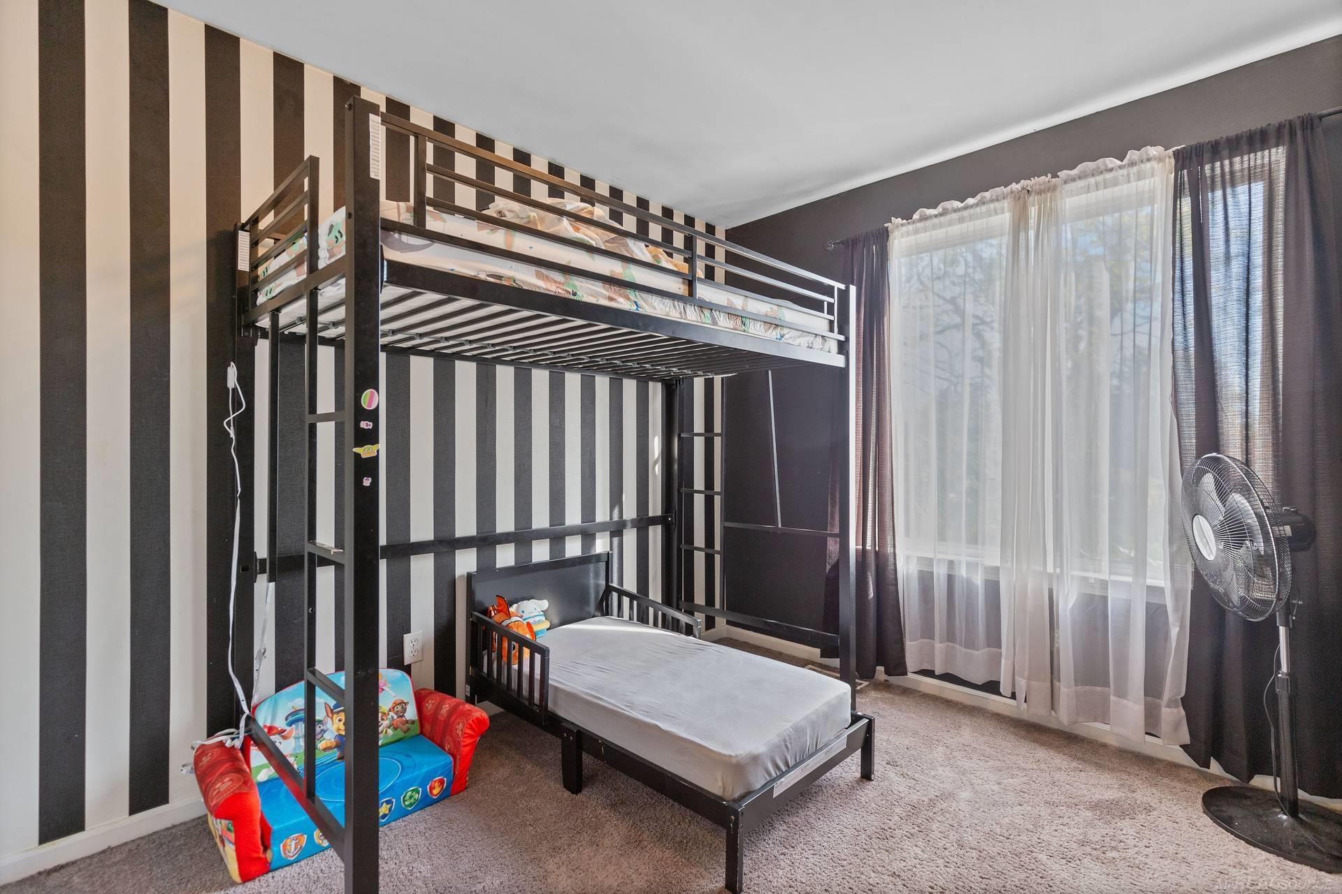 Bedroom with black metal bunk beds, striped walls, and a colorful children's play couch.