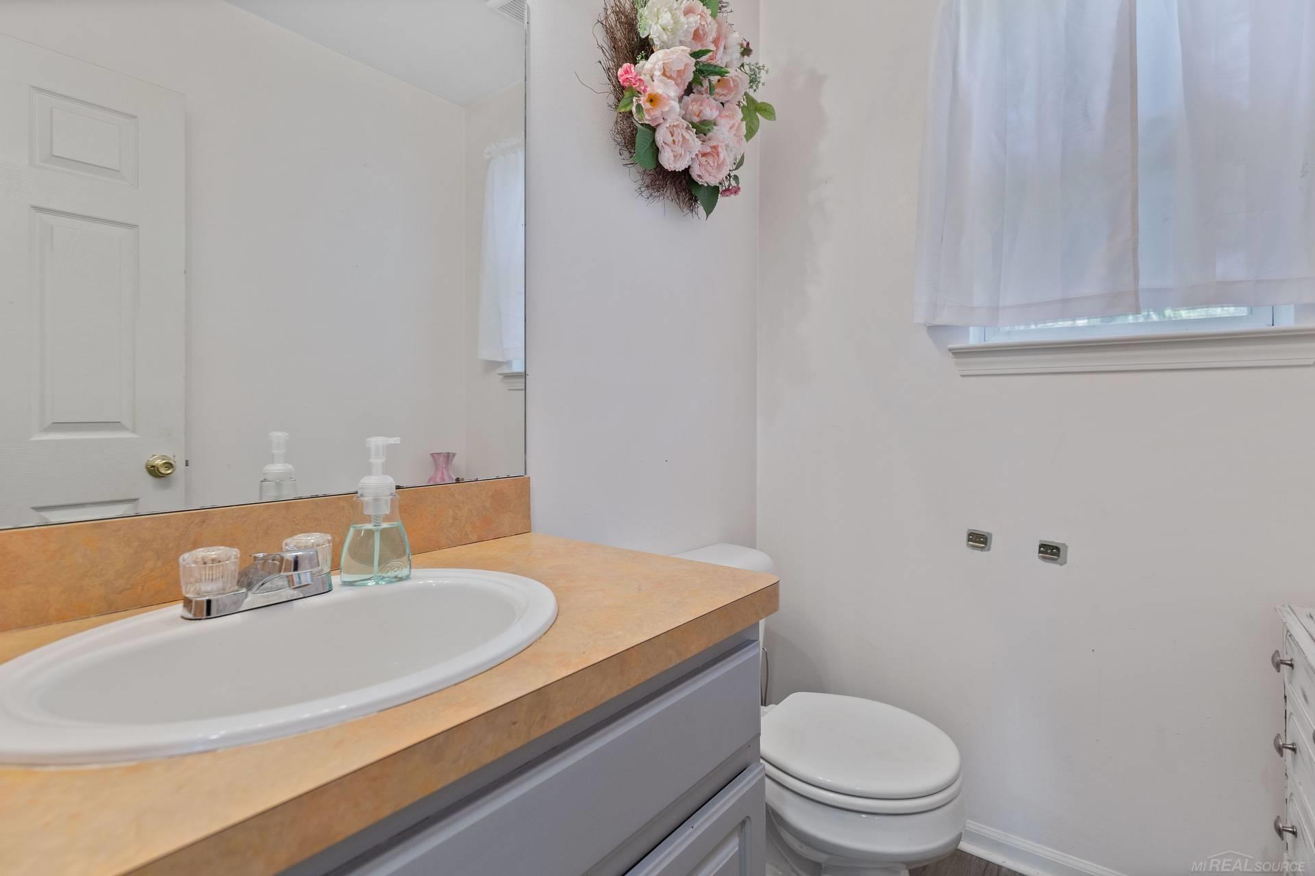 Bathroom with a peach countertop, gray vanity, white sink and toilet, and curtained window.
