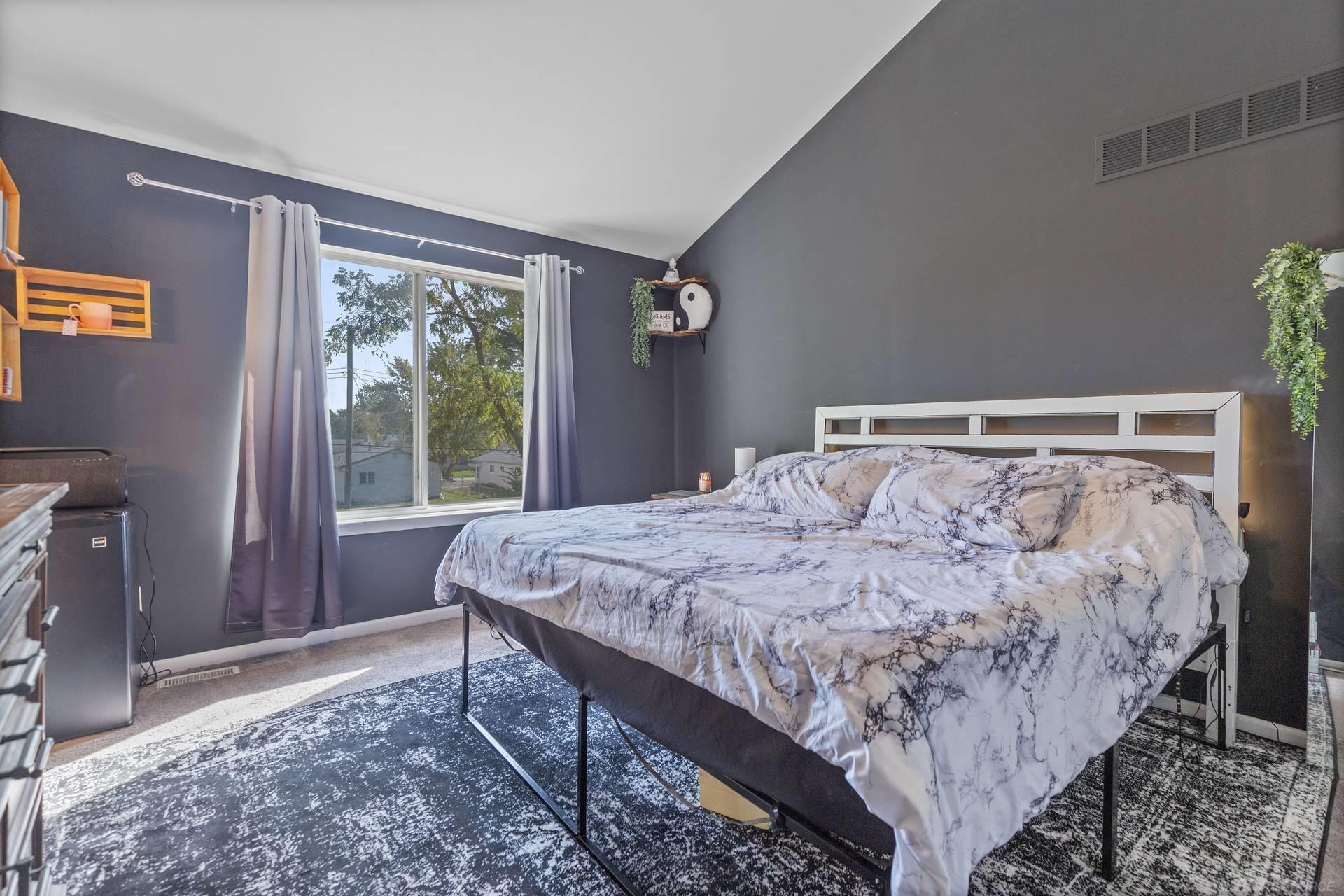 Furnished bedroom with a marble-pattern bedspread, dark walls, and a curtained window.