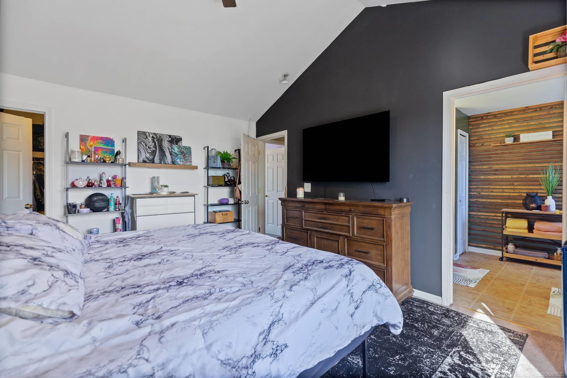 Bedroom with marble-patterned bedding, a charcoal accent wall, and a mounted television.