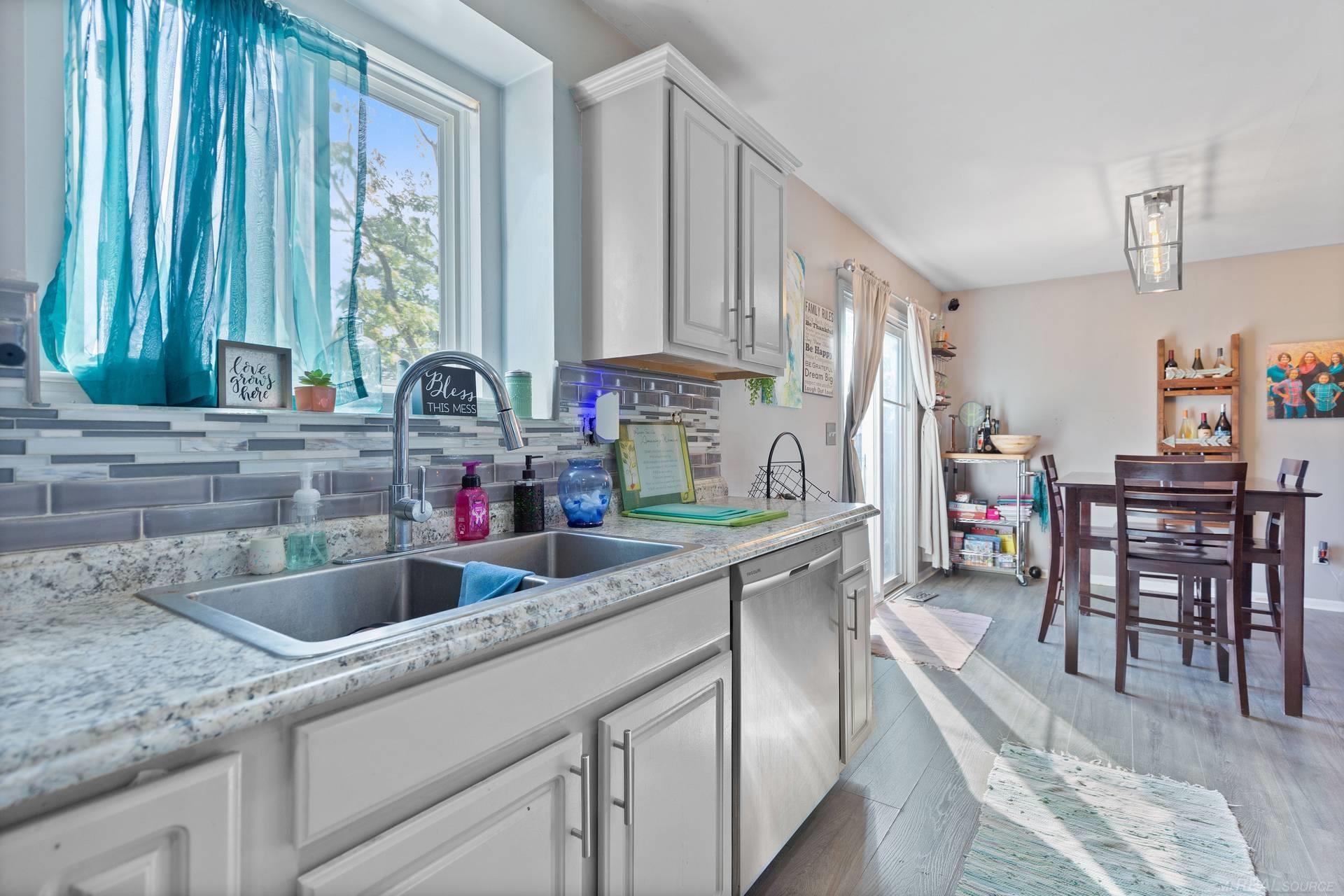 Kitchen and dining area with a granite counter, double sink, turquoise curtains, and dark wood table.