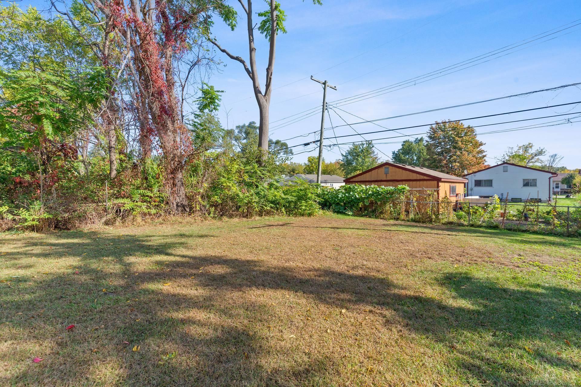 Grassy backyard bordered by mature trees, dense vegetation, and a fence.