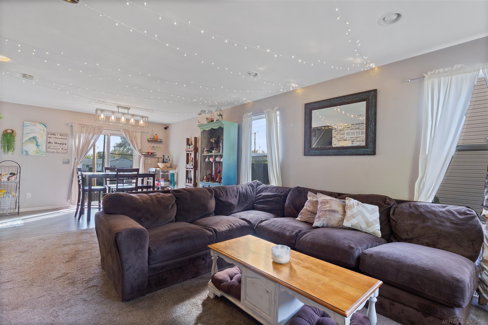 Living room with a large dark sectional, dining area, turquoise cabinet, and string lights across the ceiling.