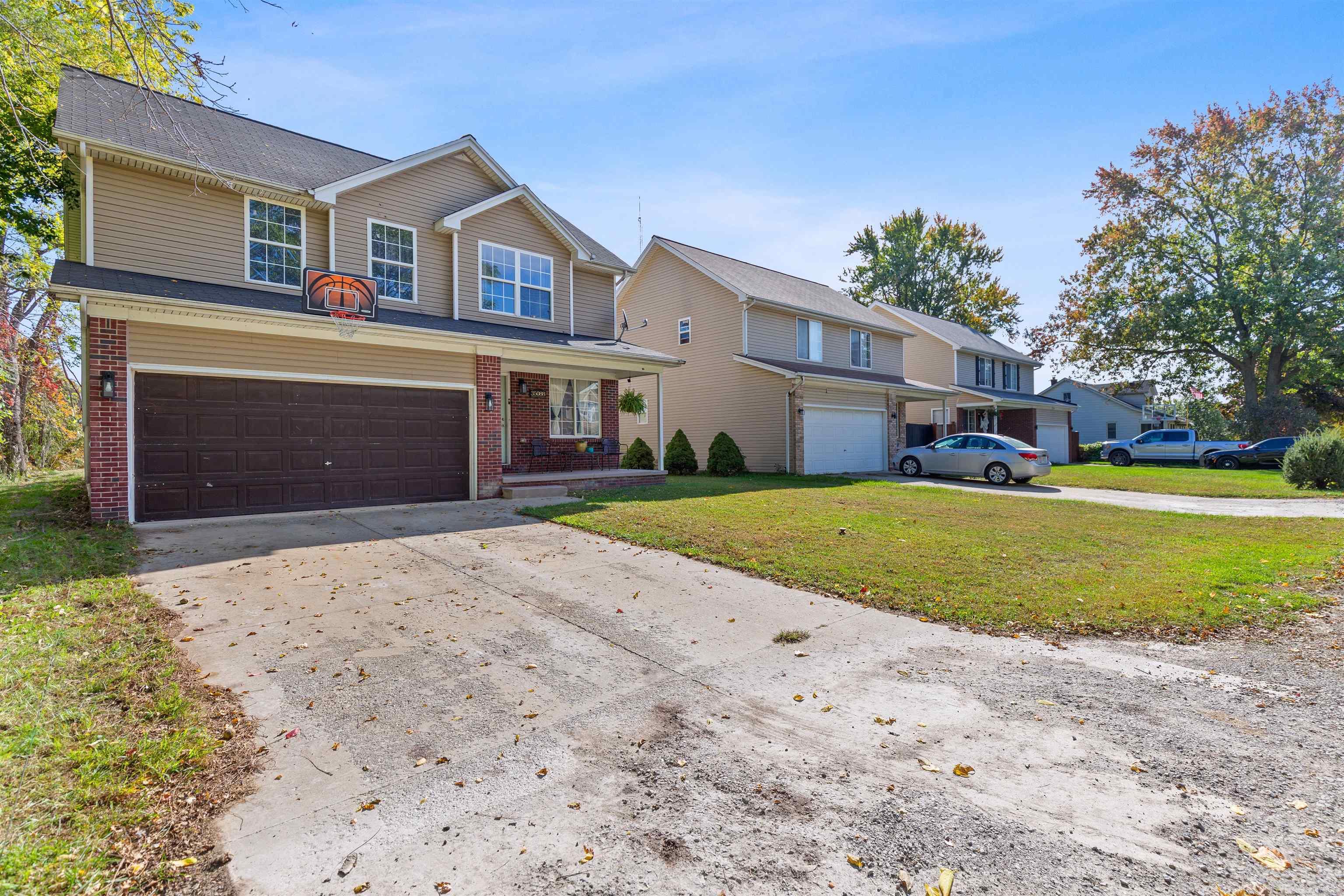Two-story tan house with brick accents, a double garage, and a basketball hoop above the driveway.