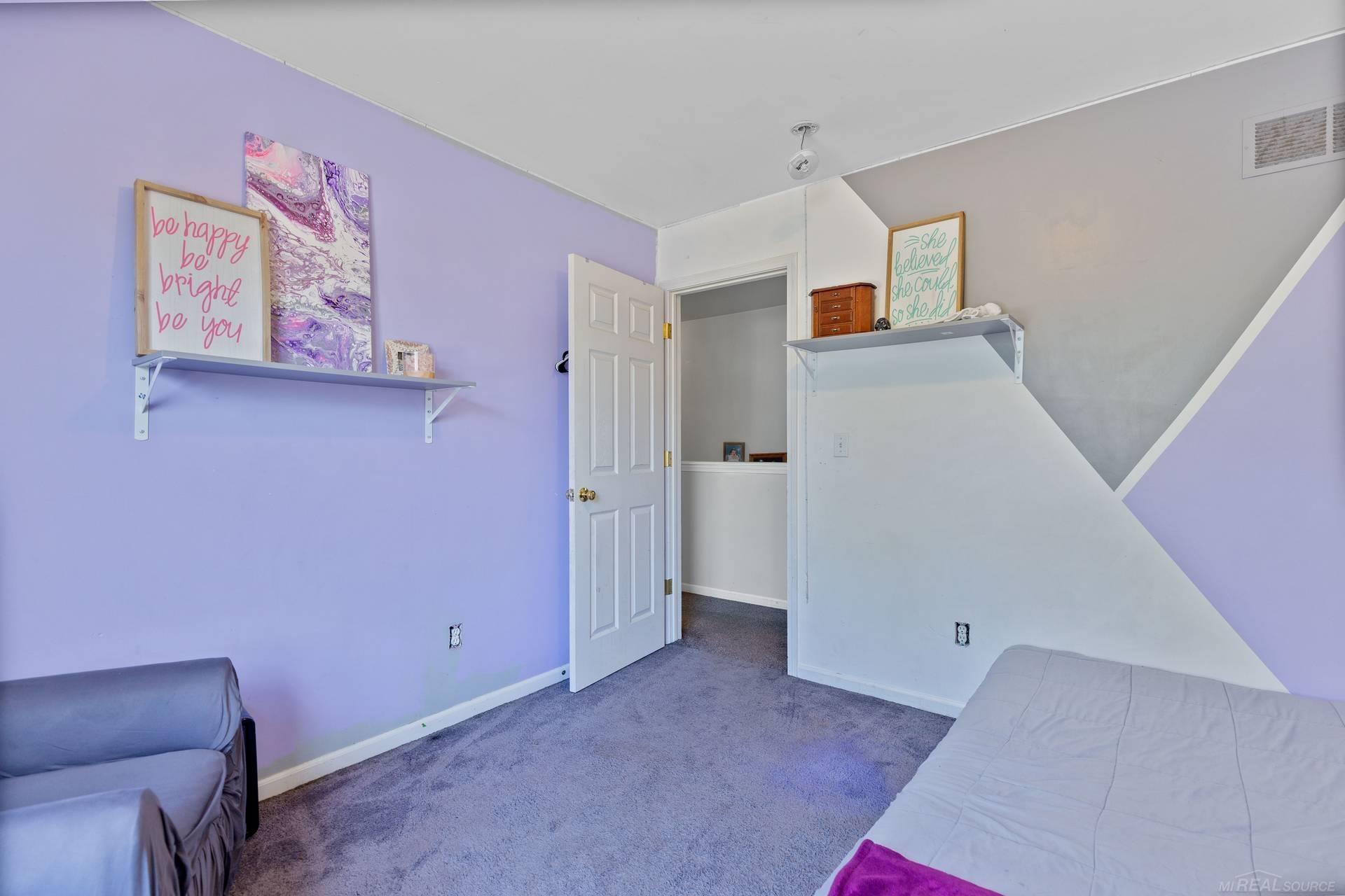 Bedroom with lavender walls, a geometric accent wall, gray carpet, and wall shelves.