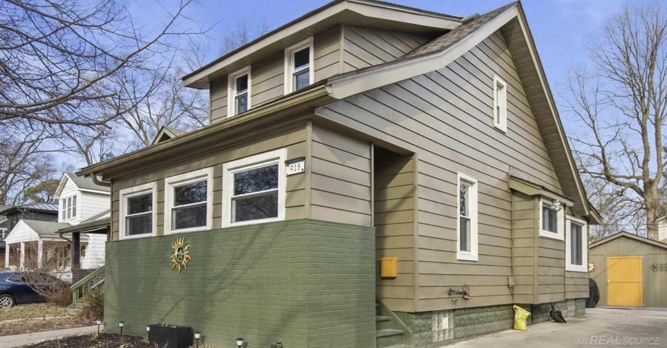 Two-story beige house with green brick lower facade, white-trimmed windows, and a yellow garage door.