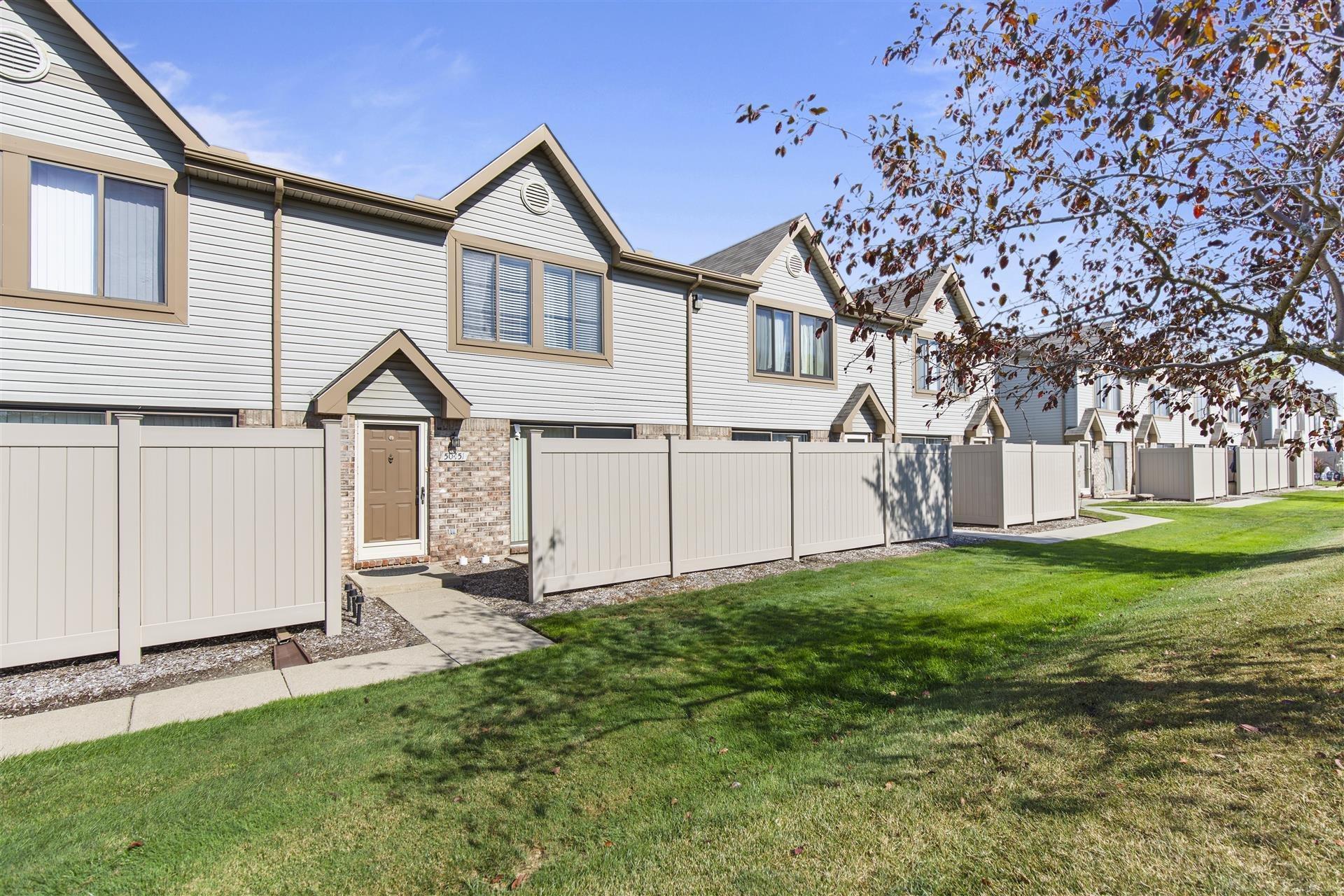 Row of gray-sided townhomes with fenced patios, a green lawn, and autumn leaves.