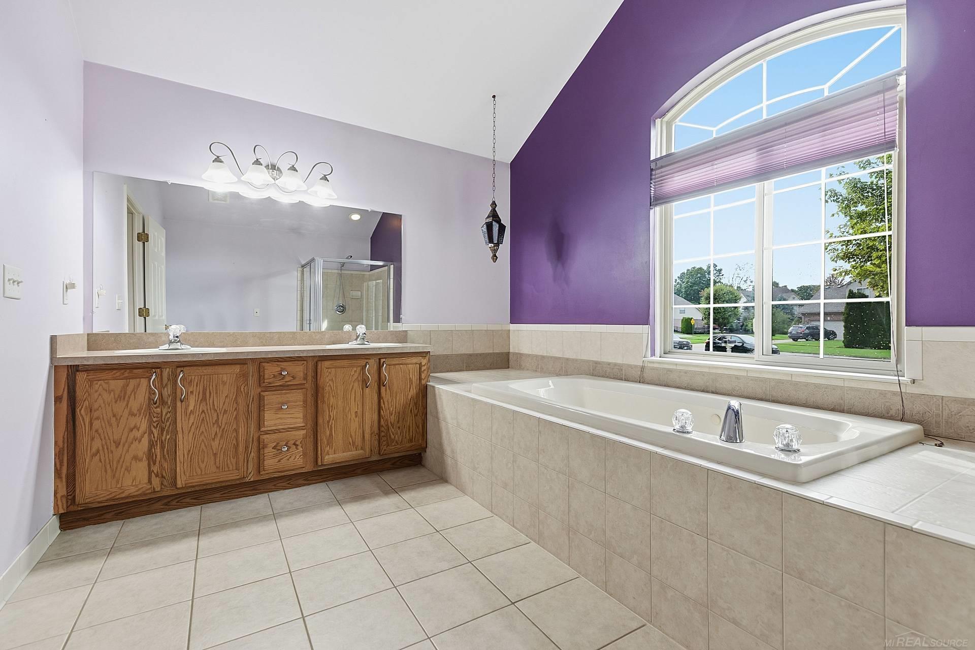 Bathroom with a tiled soaking tub beneath an arched window and a long wood double vanity.