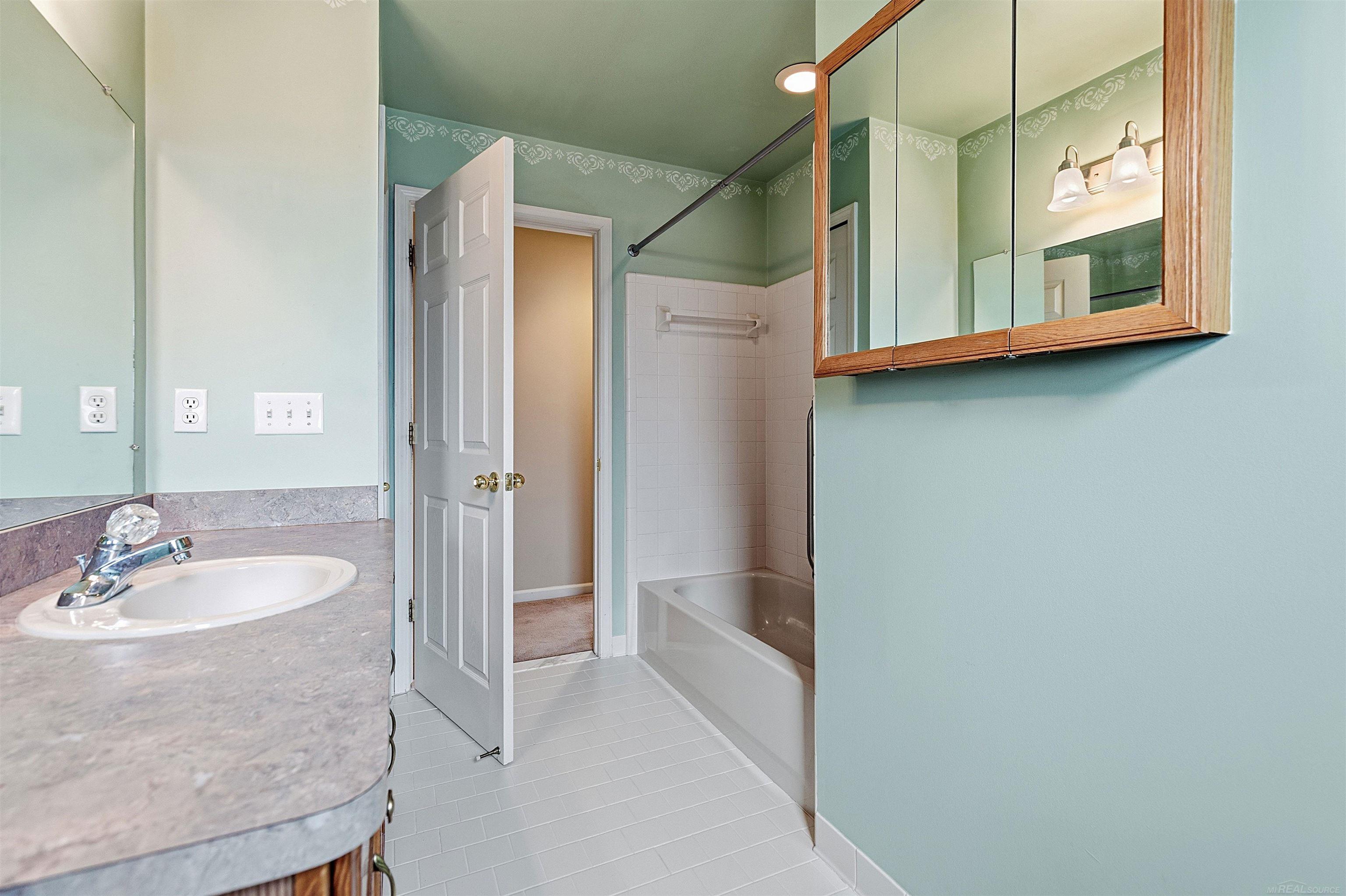 Bathroom with a white tub, vanity sink, and wood-framed mirrored medicine cabinet.