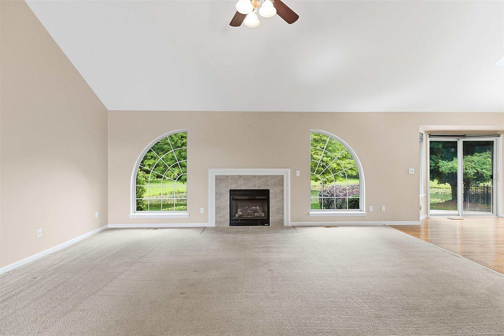 Empty living room with a tiled fireplace between arched windows and sliding glass doors.